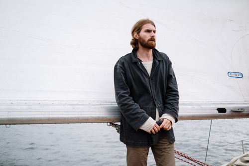Free A fashionable man standing on a yacht deck with a sail backdrop, exuding nautical style. Stock Photo