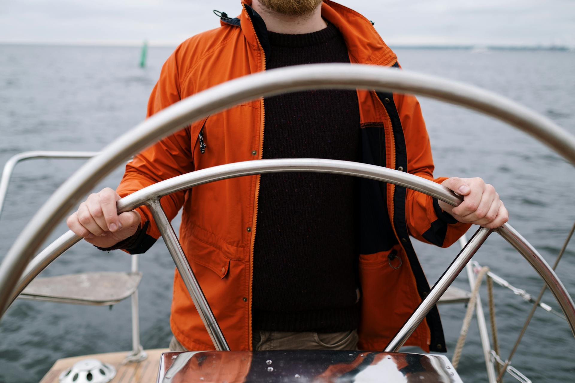 Close-up of a captain steering a boat in the sea, wearing an orange jacket.