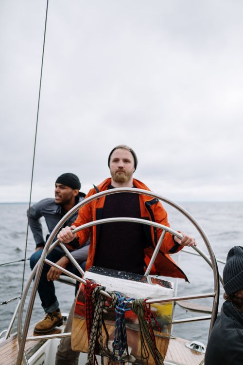 Free Three men steering a sailing boat together on an open sea, exemplifying teamwork and adventure. Stock Photo