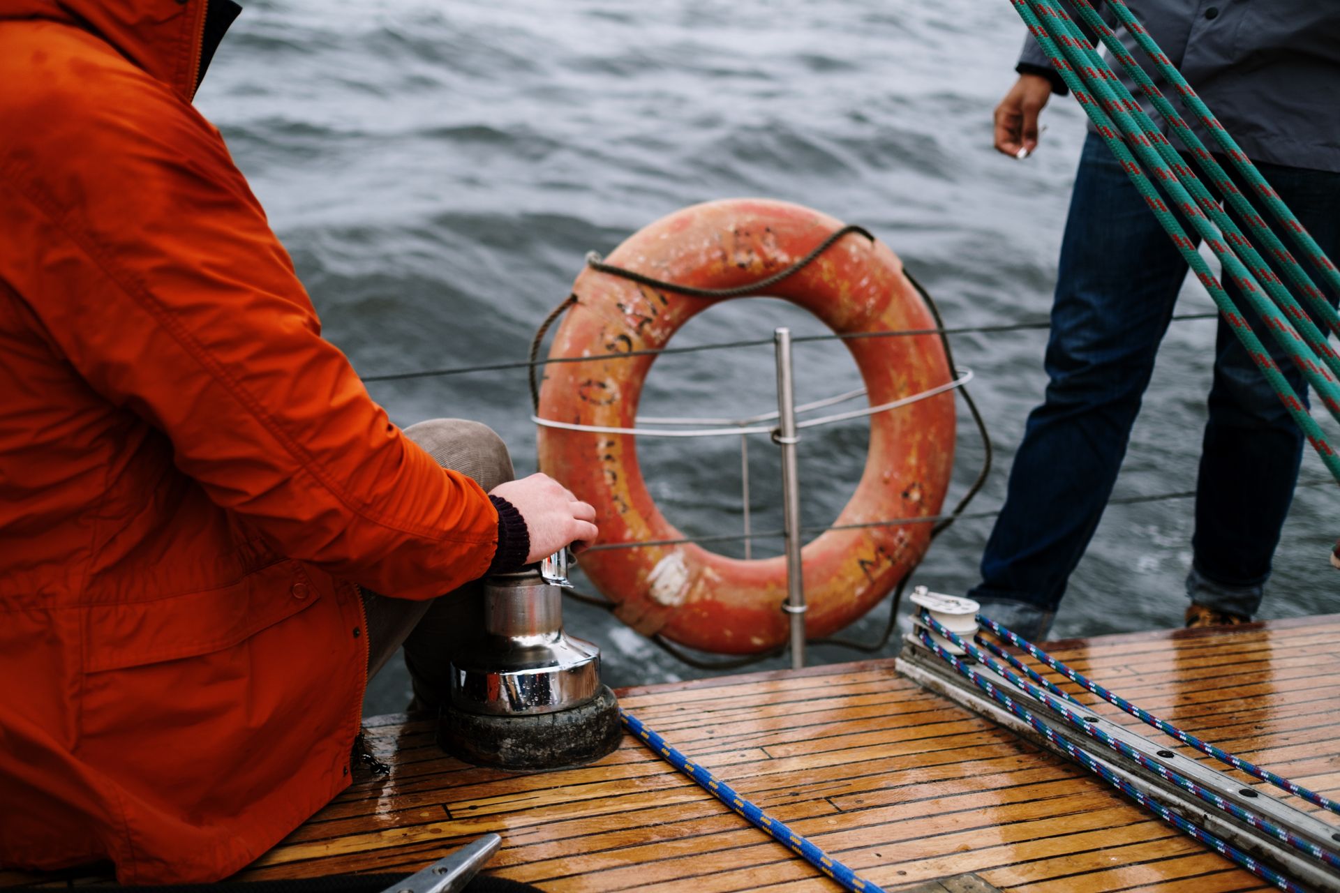 Close-up of two men navigating a sailboat, emphasizing safety with a lifebuoy at sea.