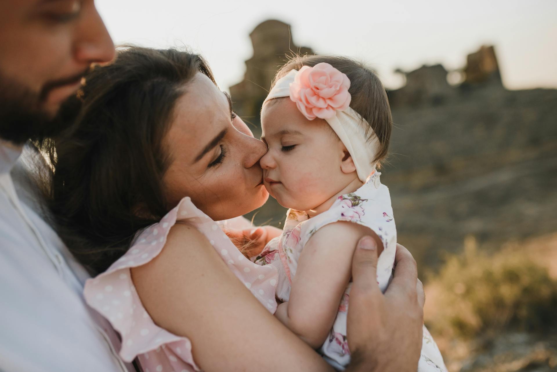 A family shares a tender moment with their baby in a sunlit rural landscape.