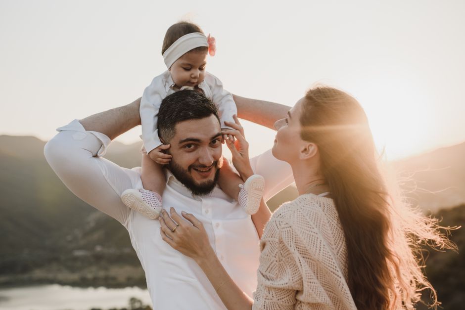 Un momento familiar alegre con los padres sosteniendo a su bebé al aire libre durante el atardecer.