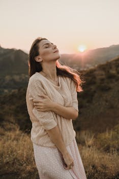 Woman with eyes closed embracing the warmth of sunset in a scenic outdoor setting.