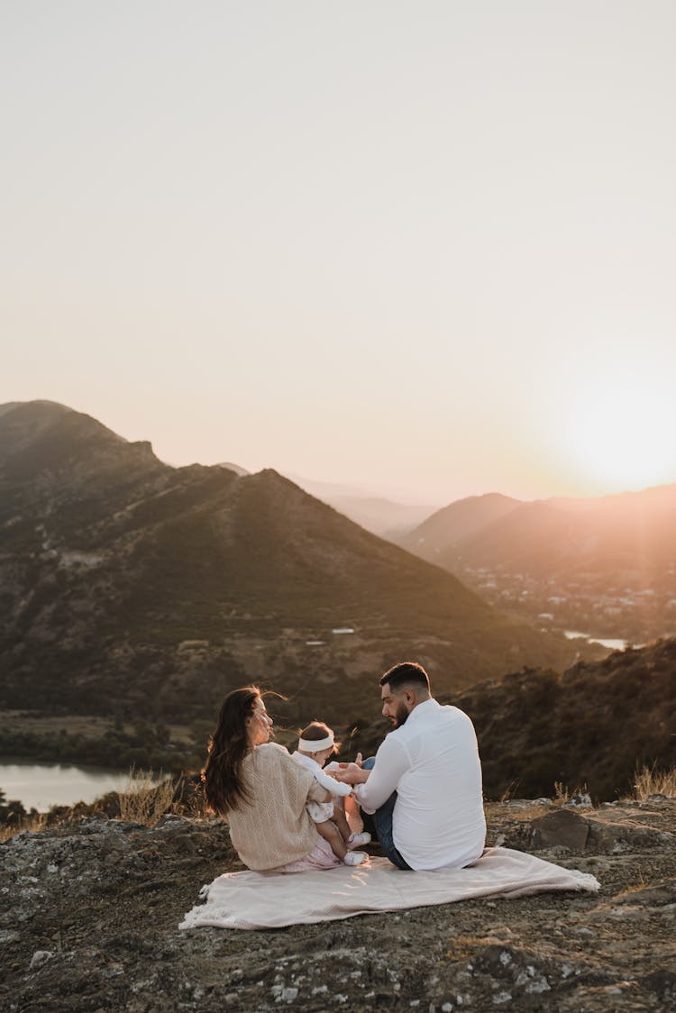 Parents Sitting With Baby On Picnic At Sunset