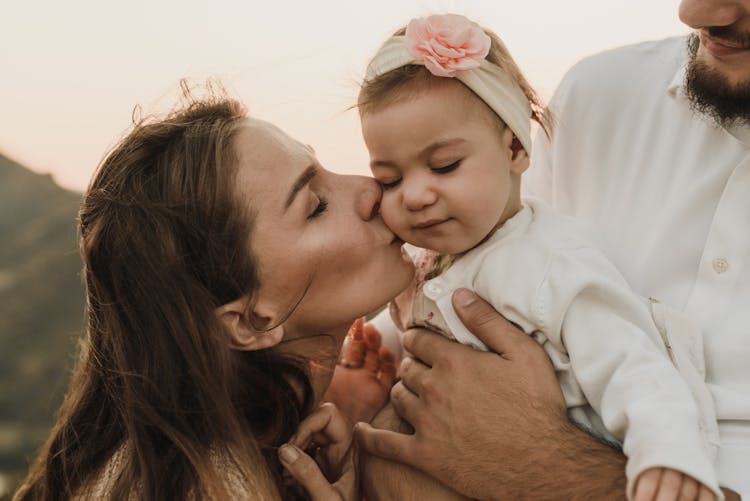 Happy Parents Hugging And Kissing Baby