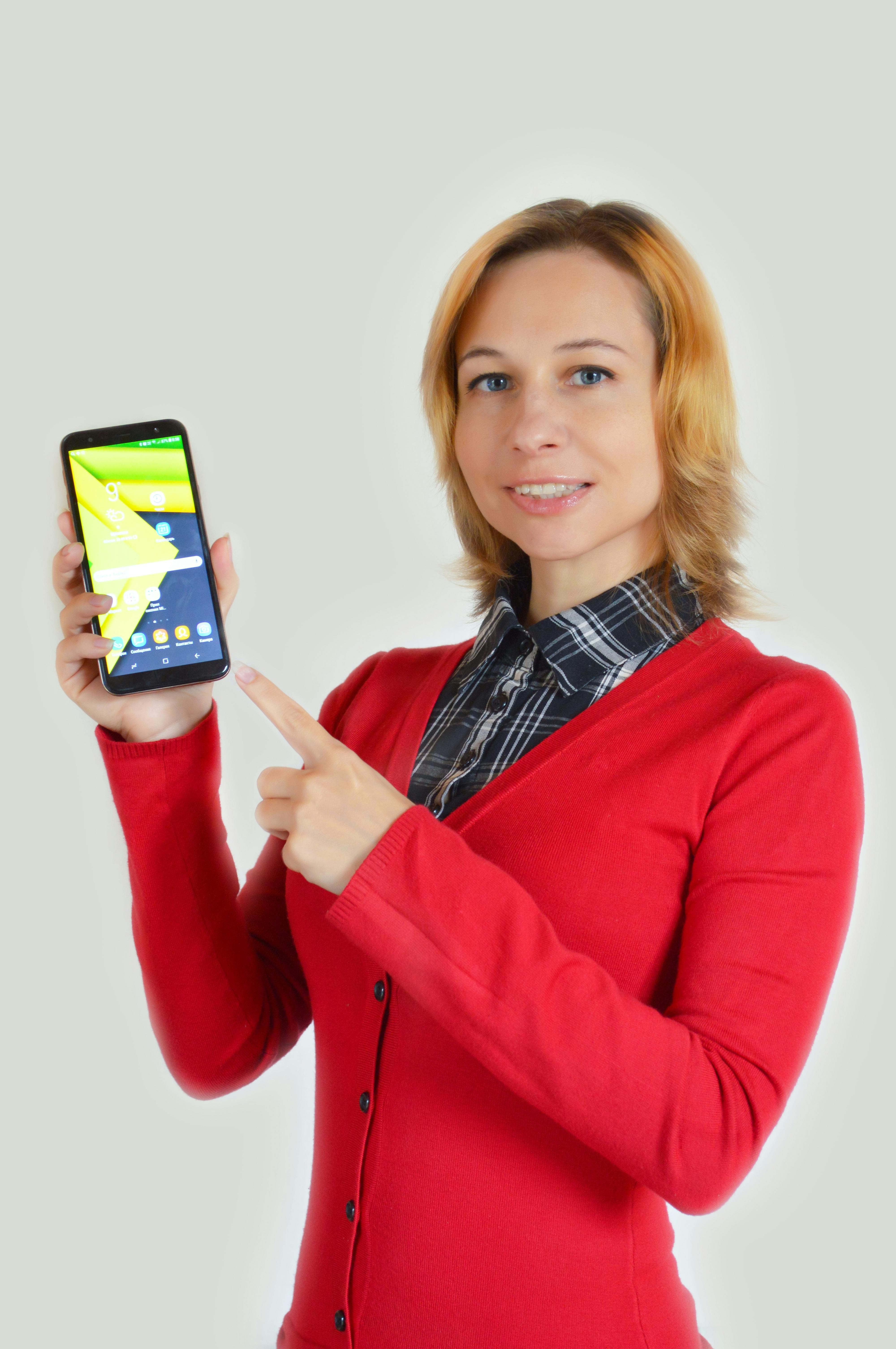 cheerful woman demonstrating smartphone and looking at camera