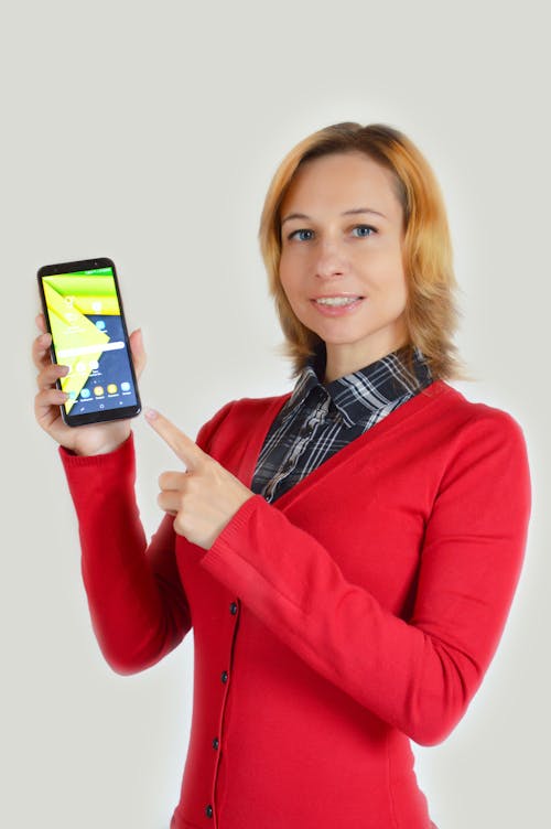 Cheerful woman demonstrating smartphone and looking at camera