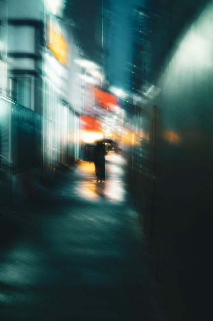 Back view of anonymous female with umbrella strolling on walkway between buildings in city illuminated by shiny lights at night