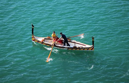 Free Aerial view of two men rowing a vibrant boat on turquoise waters. Bright, adventurous, and serene. Stock Photo