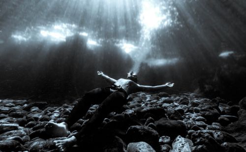 Free Monochrome photograph of a man floating underwater on a rocky sea bed, illuminated by sunlight. Stock Photo