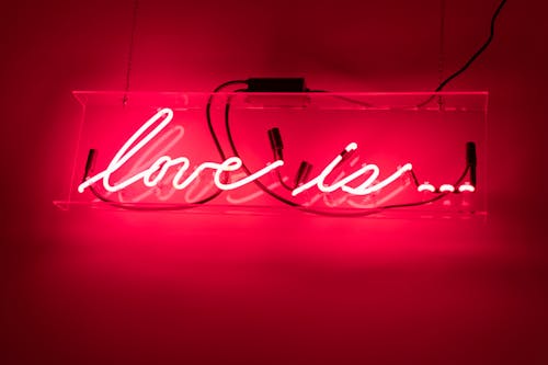 Colorful red signboard with shiny Love Is title behind wires on house wall in evening