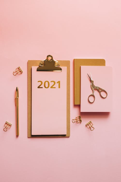 Top view of golden clipboard and accessories with pink colored papers and 2021 year