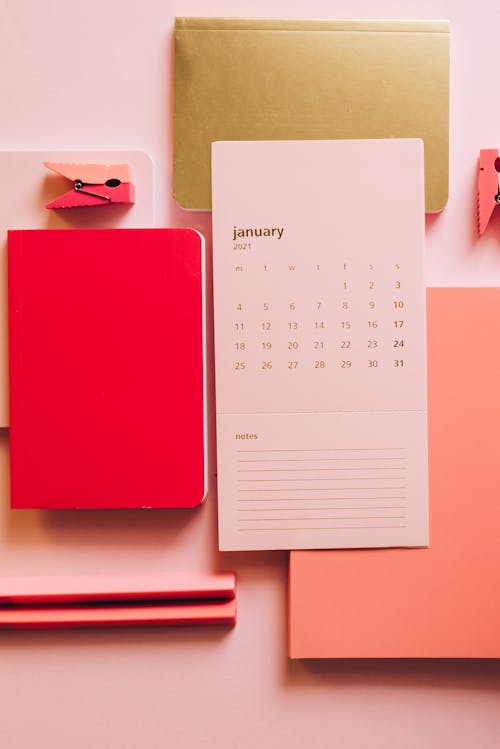Flat lay of pink sheet with January month calendar and pink notepads with pins