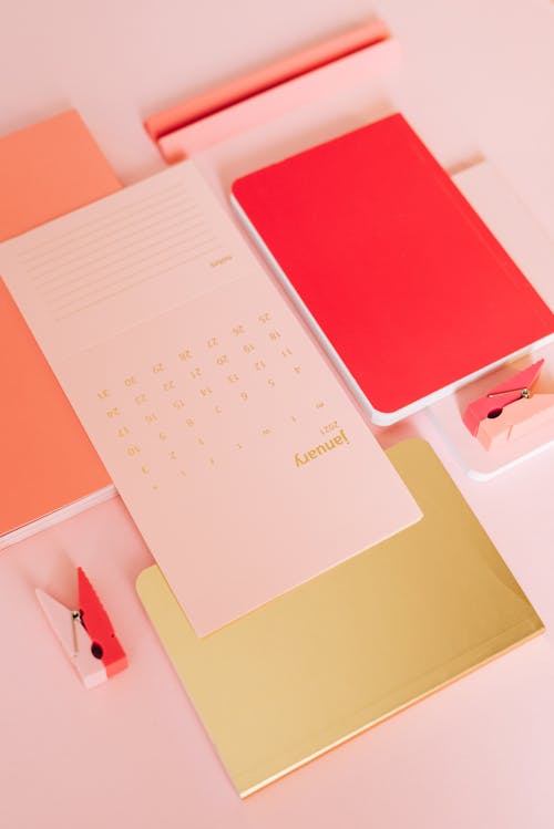 Layout of stylish notebooks with calendar paper and wooden clips on pink background