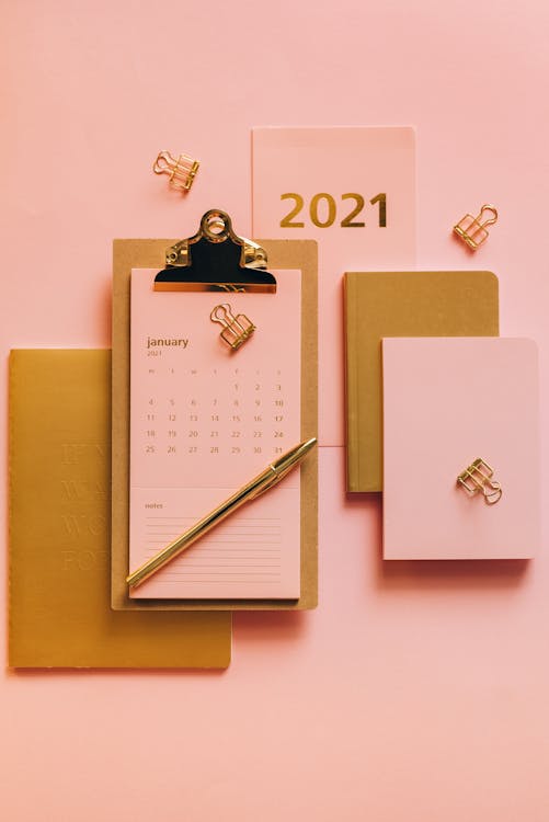 From above minimalistic composition of clipboard with calendar surrounded modern stationery on pink background