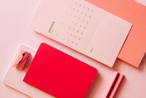 Layout of calendar paper with notes on bright multicoloured notebooks on pink background