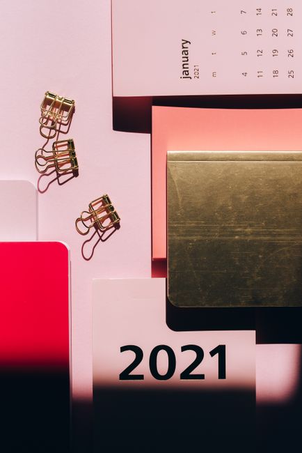 From above colorful notepads with calendar arranged with golden paper clips on pink background