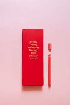 Red calendar featuring days of the week with a pink pen on a soft pink background, minimal design.