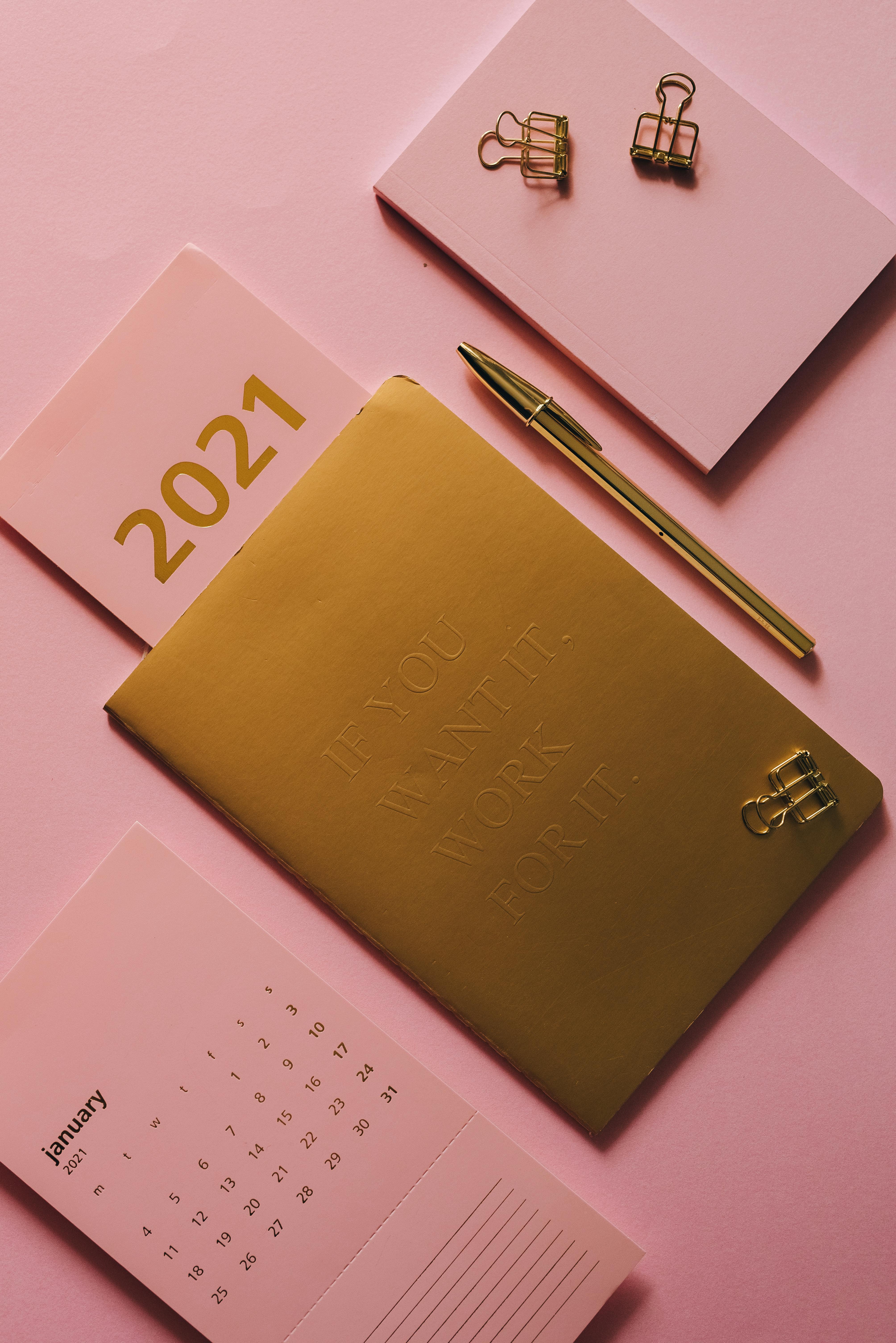 notebook pen and calendar on pink background