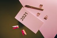 办公用品的扁平布局中，包括2021年日历卡、钢笔和粉色背景上的夹子