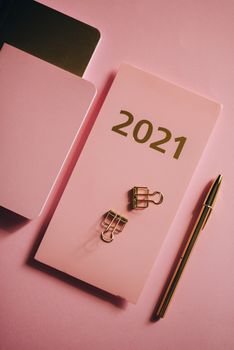 一份2021年计划书铺在粉色背景上，上面别着金色的曲别针和笔