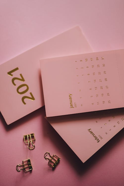 Modern calendars near metal clips on pink background