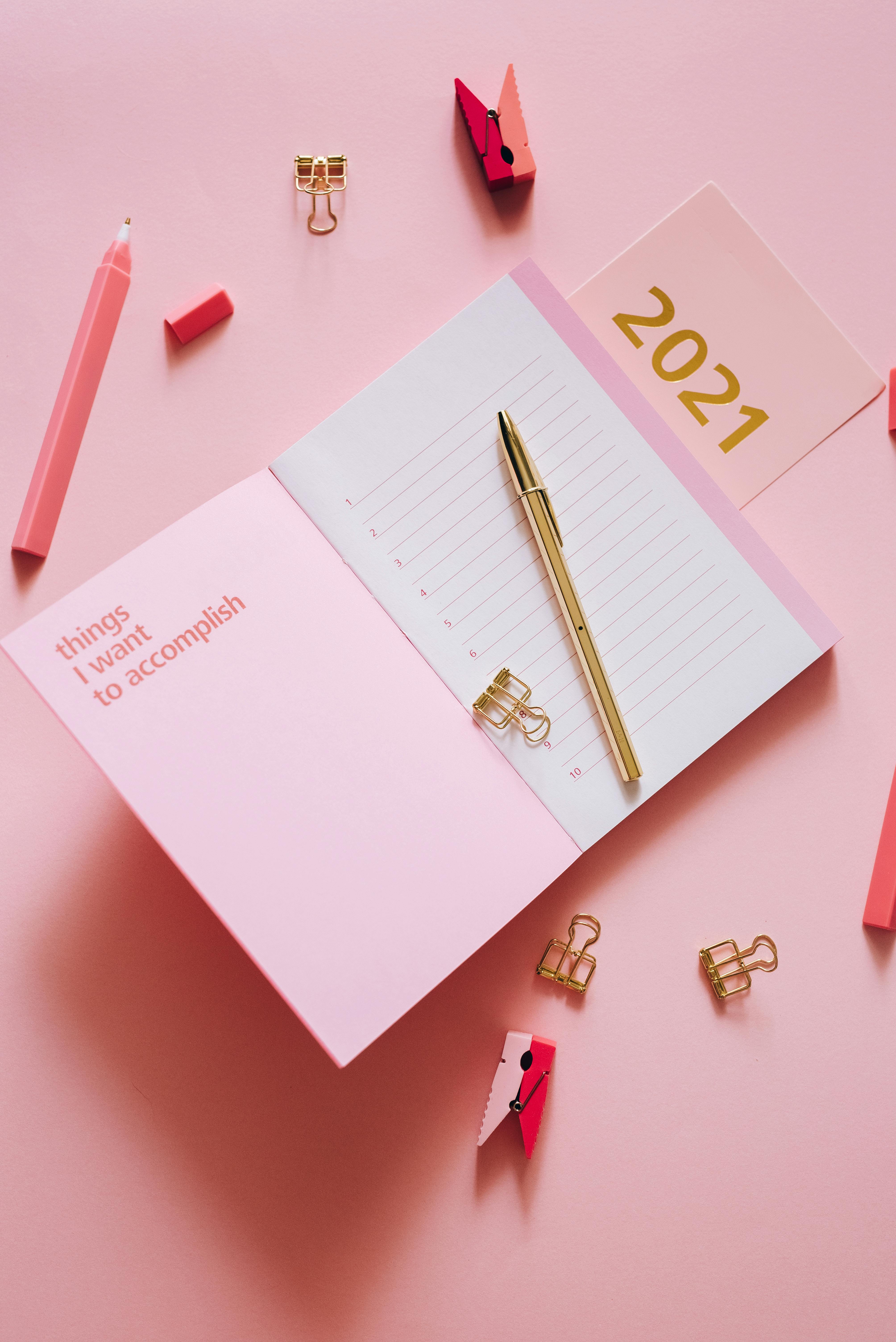 close up of notebook with pen on pink background