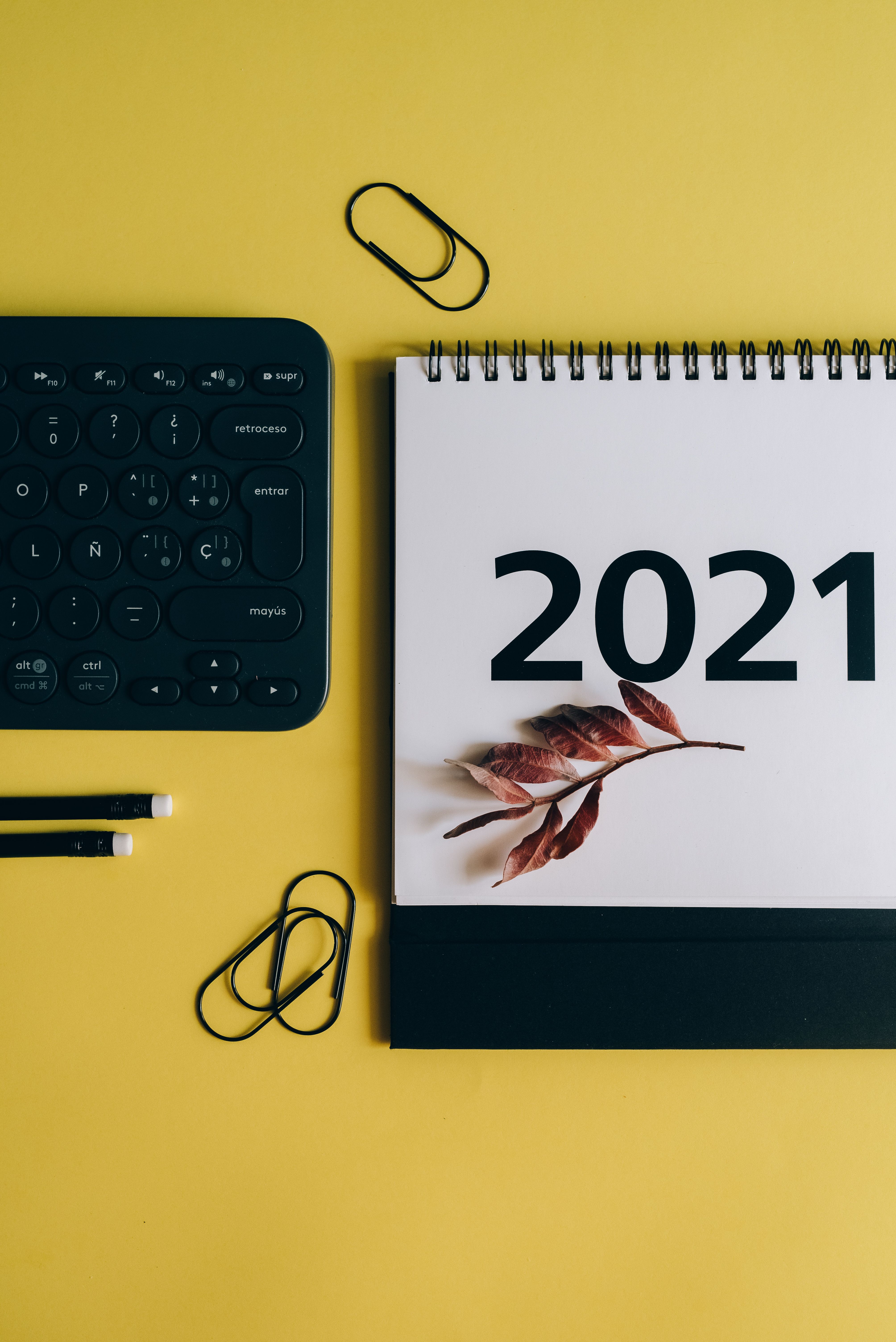 2021年日历的顶视图以黄色为背景，上面点缀着秋叶，旁边还配有键盘和文具