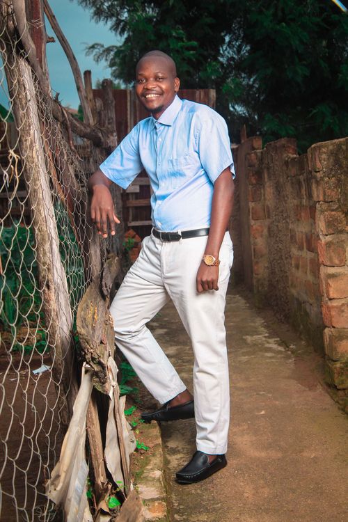 Free A cheerful man stands outdoors by a rustic fence, casually dressed and smiling. Stock Photo