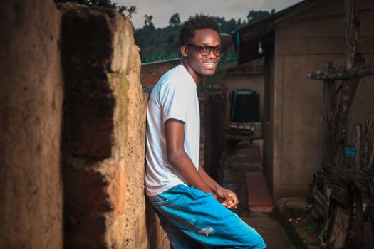 A cheerful man in casual attire leaning against a rustic urban wall on a sunny day.