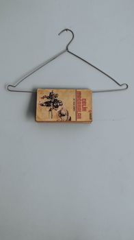 A vintage book creatively displayed on a minimalist wire hanger against a plain wall.