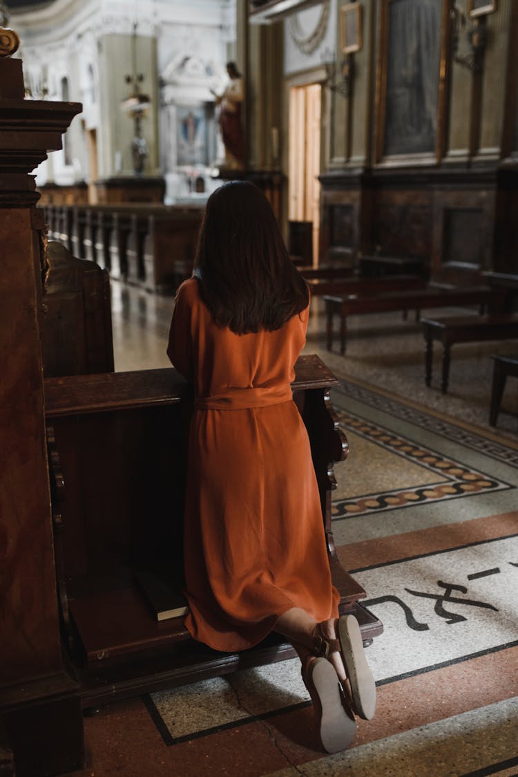 A Woman Kneeling On A Pew While Praying In The Church