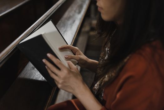 一个女人坐在教堂的长椅上，在室内全神贯注地看书