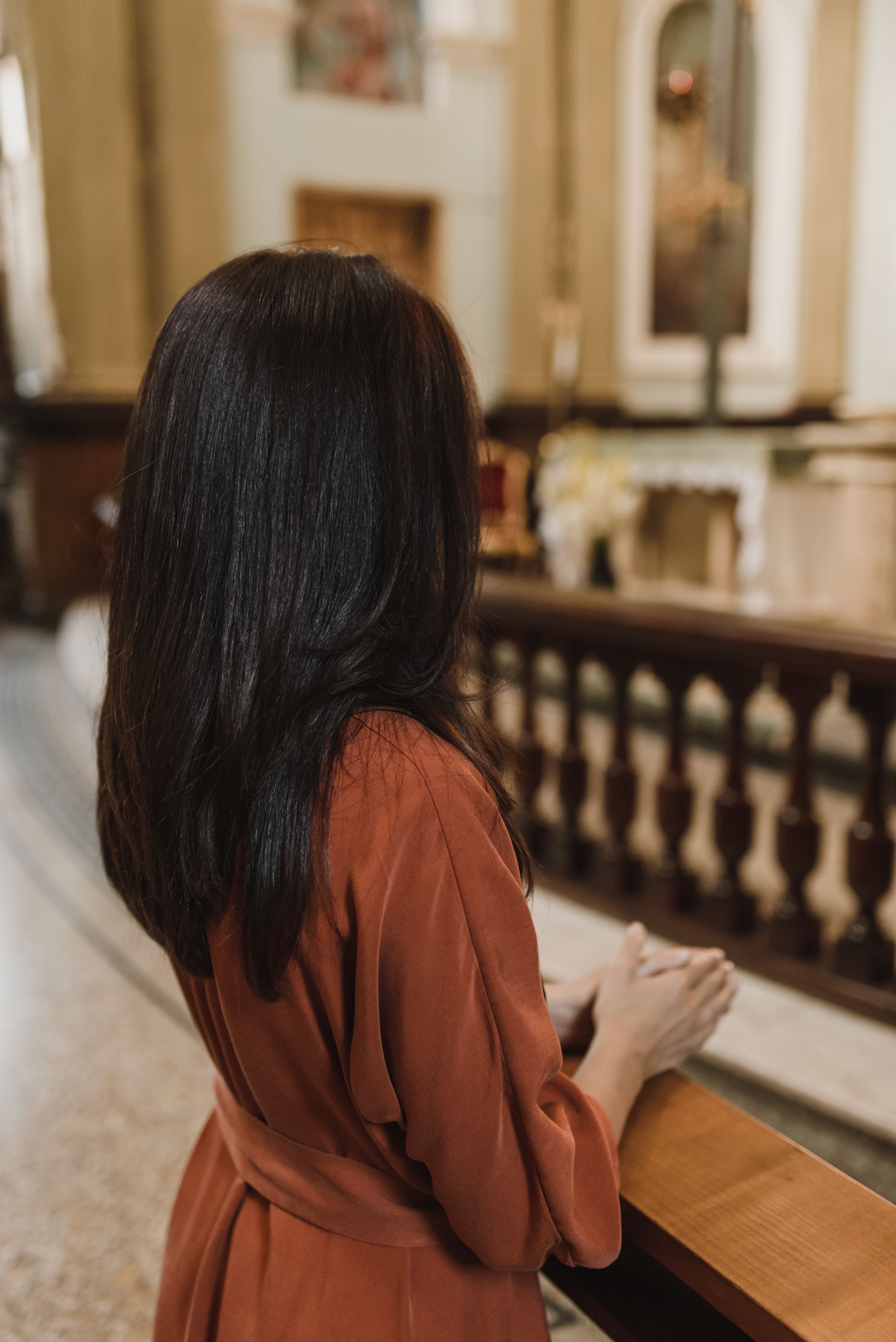 一名身穿红色连衣裙的妇女，面向祭坛，在一座宁静的教堂内祈祷