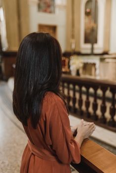 一名身穿红色连衣裙的妇女，面向祭坛，在一座宁静的教堂内祈祷