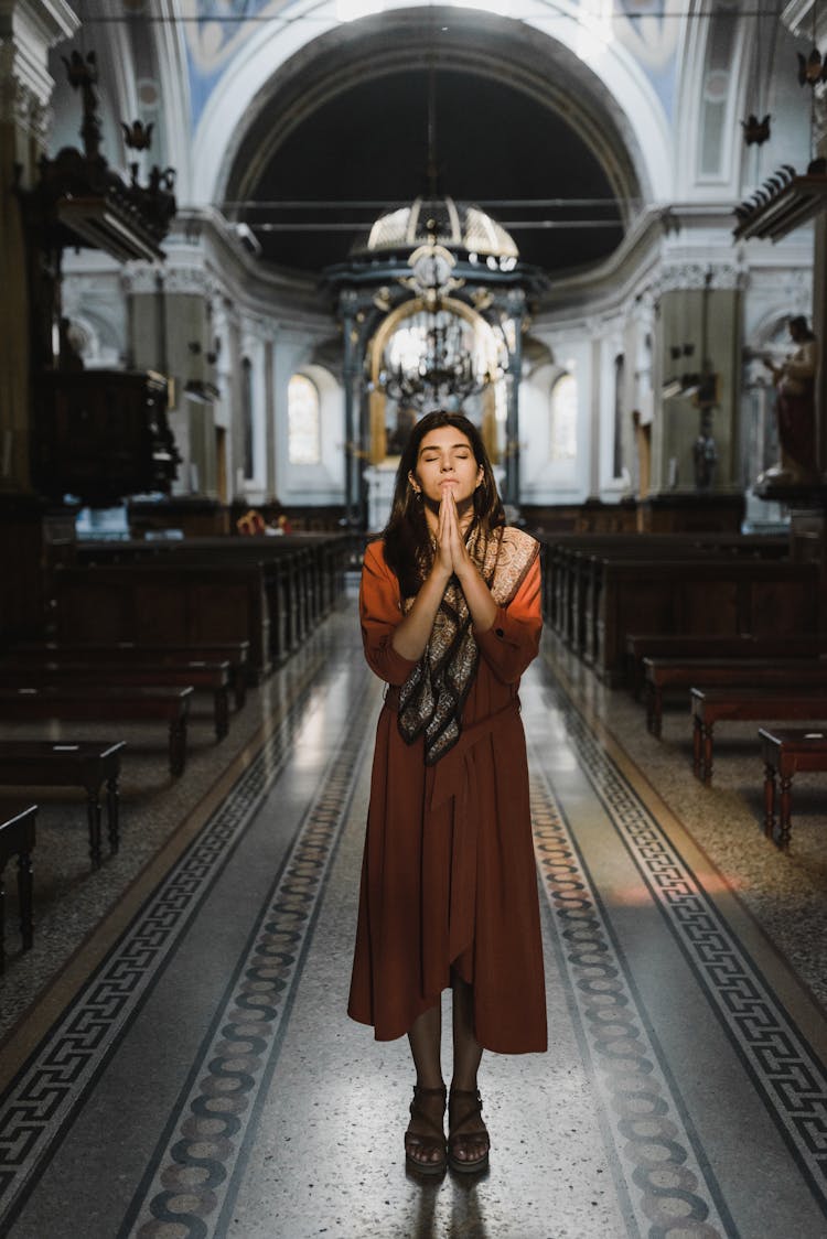 Woman In Brown Dress Standing On An Aisle With Her Hands Together