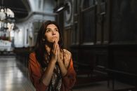 在光线昏暗的教堂里，一名妇女双手合十祈祷，营造出沉思的氛围