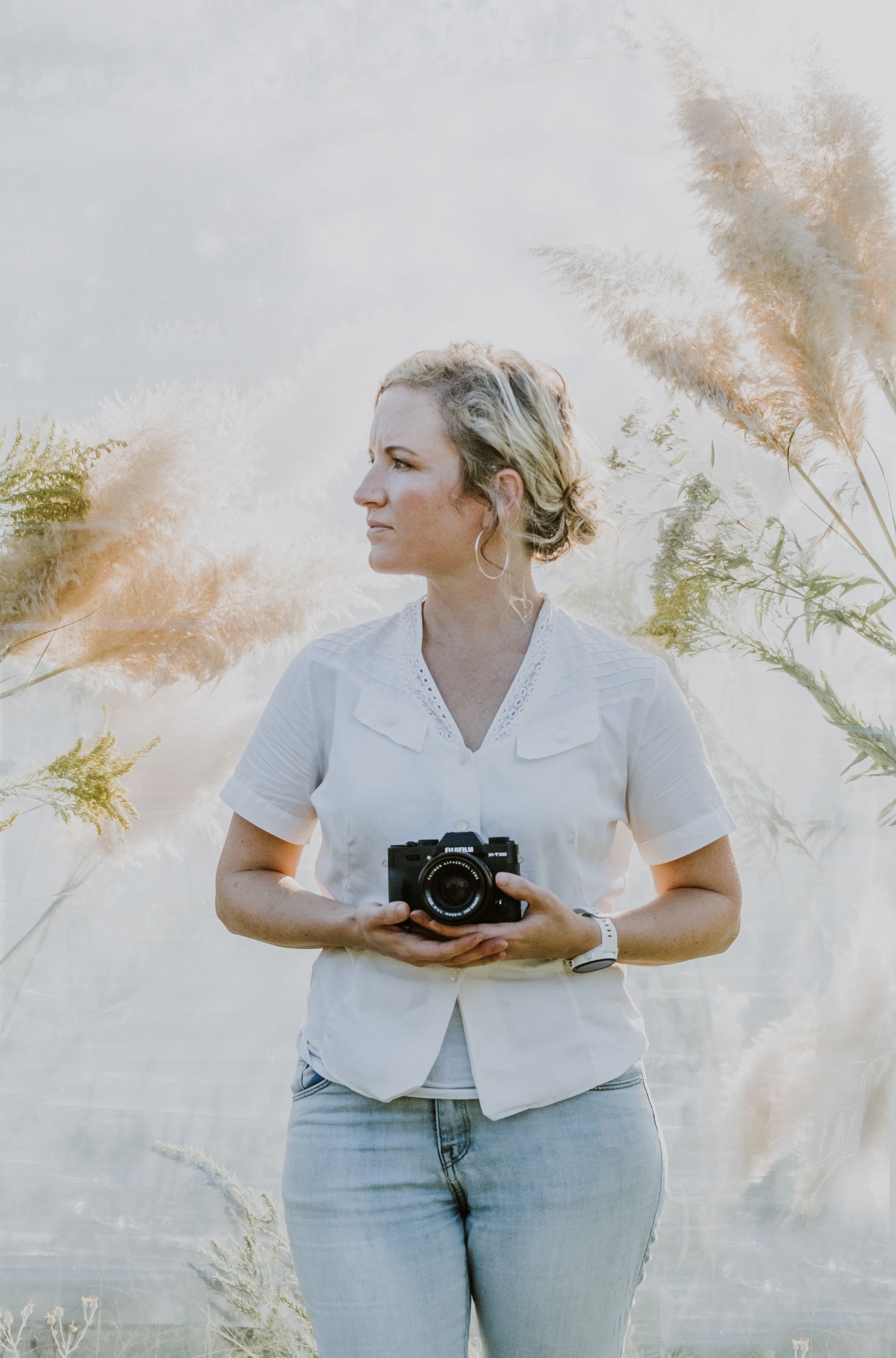 A woman holding a camera, standing amidst tall grasses, exuding a serene and natural vibe.