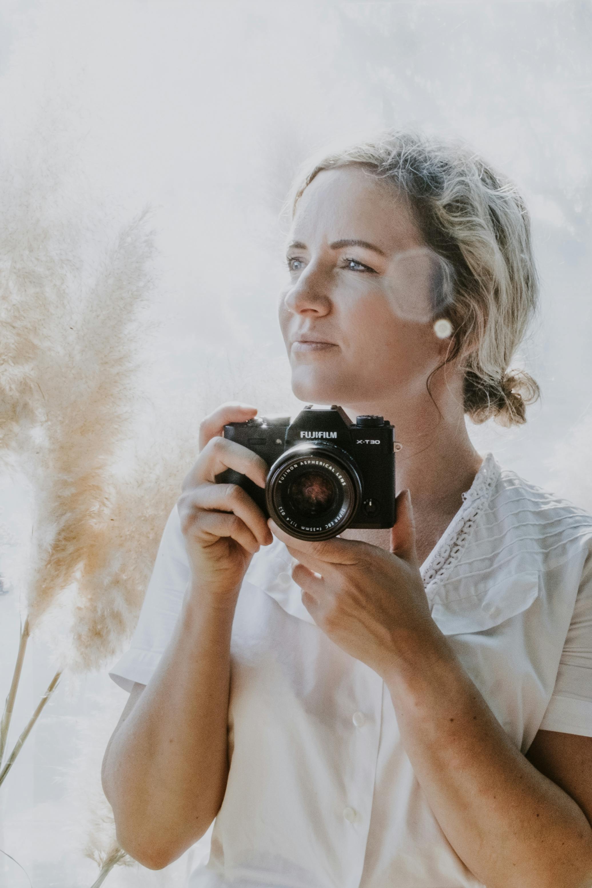 Portrait of a woman holding a camera, basking in soft natural light with pampas grass.