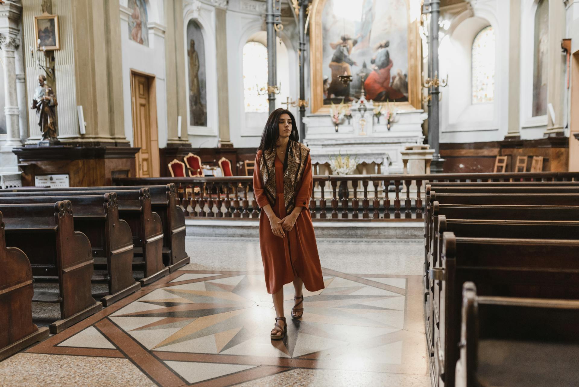 A woman gracefully walks down the aisle of a beautifully lit historic cathedral, evoking a sense of peace.