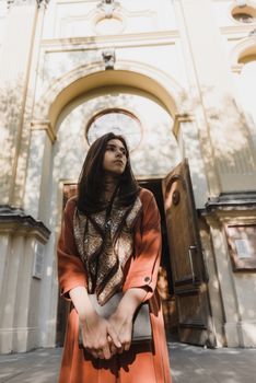 一位身着棕色连衣裙的女子，站在华丽的教堂门口，正以沉思的姿态眺望远方