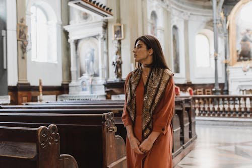 A Woman in Brown Long Sleeve Dress Walking Beside the Pews 