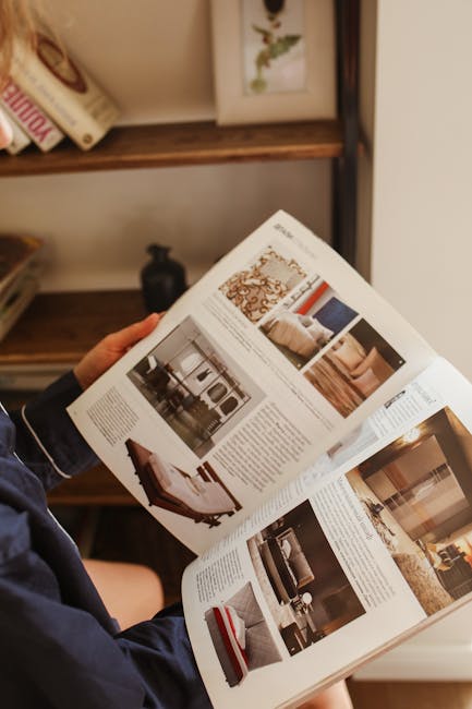 Hands holding and reading a home decor magazine indoors, showcasing interior designs.