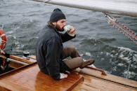 一名轻松的男子在开阔水域的帆船上享用热饮