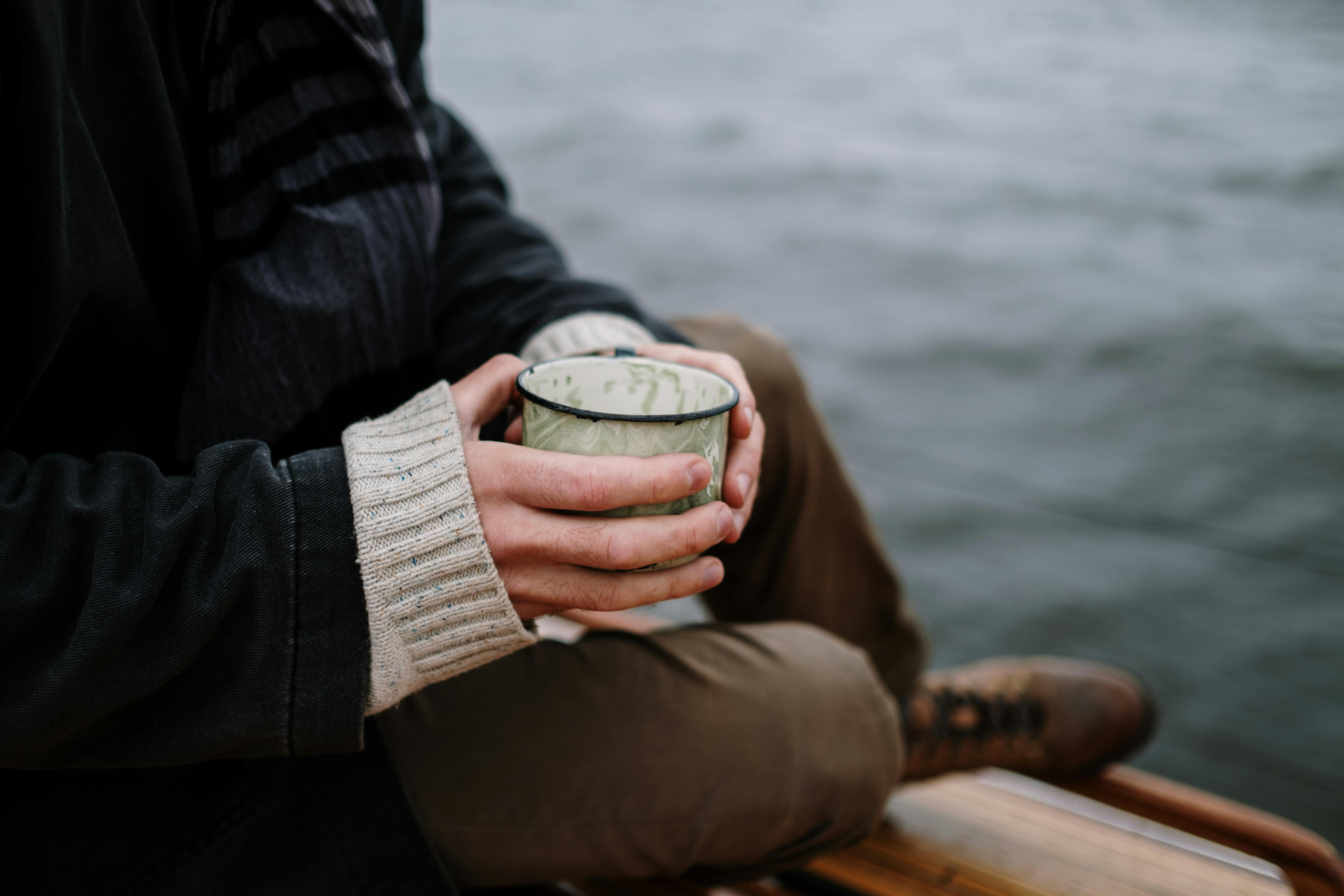 拿著白色和綠色陶瓷杯的人