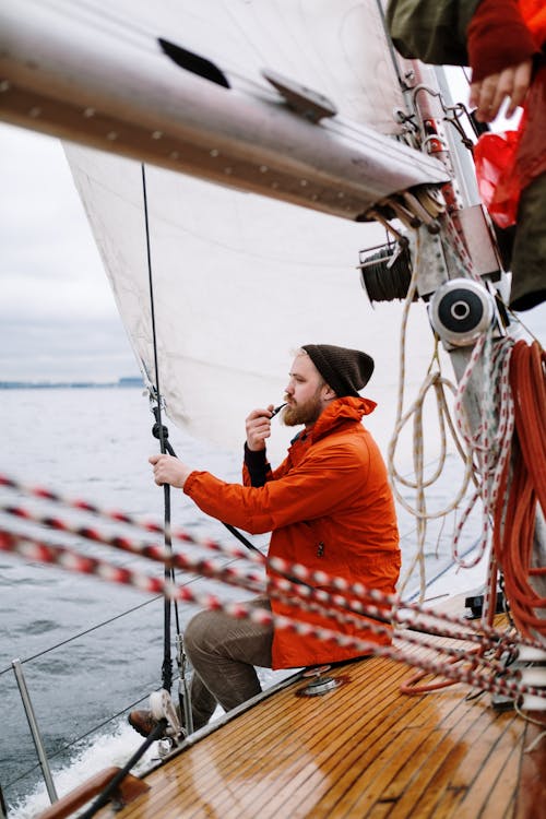 Free Man in Orange Jacket Holding a Tabaco Pipe While Sitting on the Boat Stock Photo