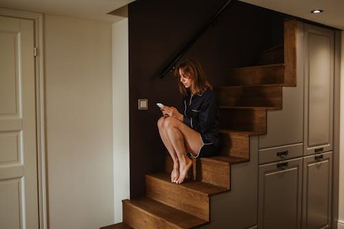 Free Woman in Blue Shirt Sitting on Brown Wooden Staircase Stock Photo