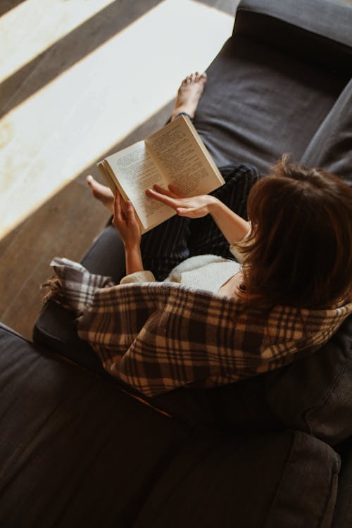 Free Woman Sitting on a Sofa and Reading a Book  Stock Photo