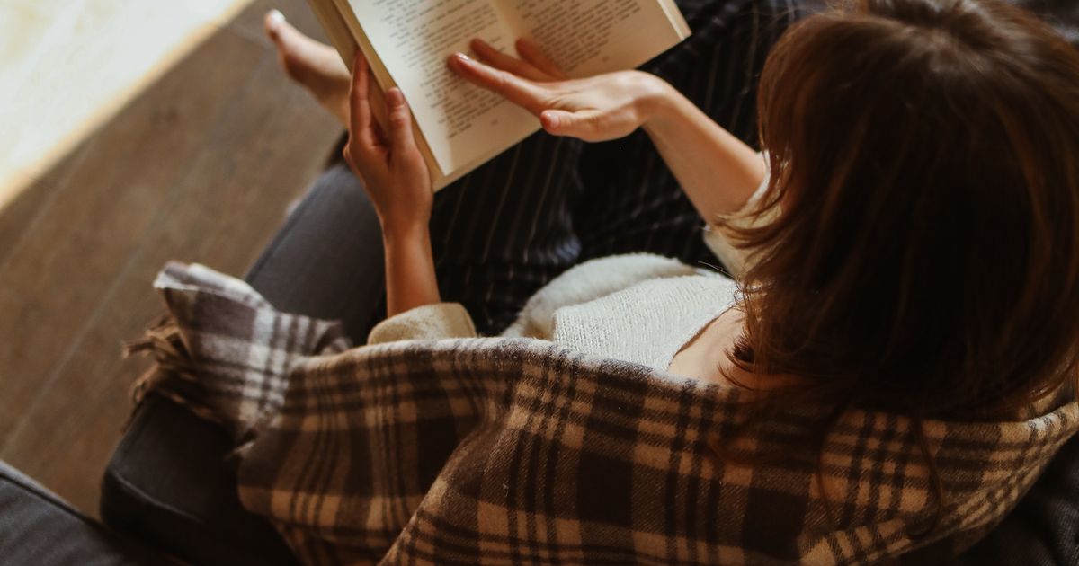 A woman relaxing in bed reading a book in a sunlit room