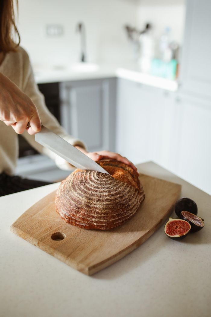 A cook slicing a round loaf beside fresh figs — photo by Polina Tankilevitch on Pexels